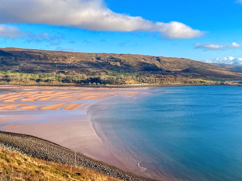Applecross Bay at low tide, ribbed sand running out into clear green water with the village along the far shore