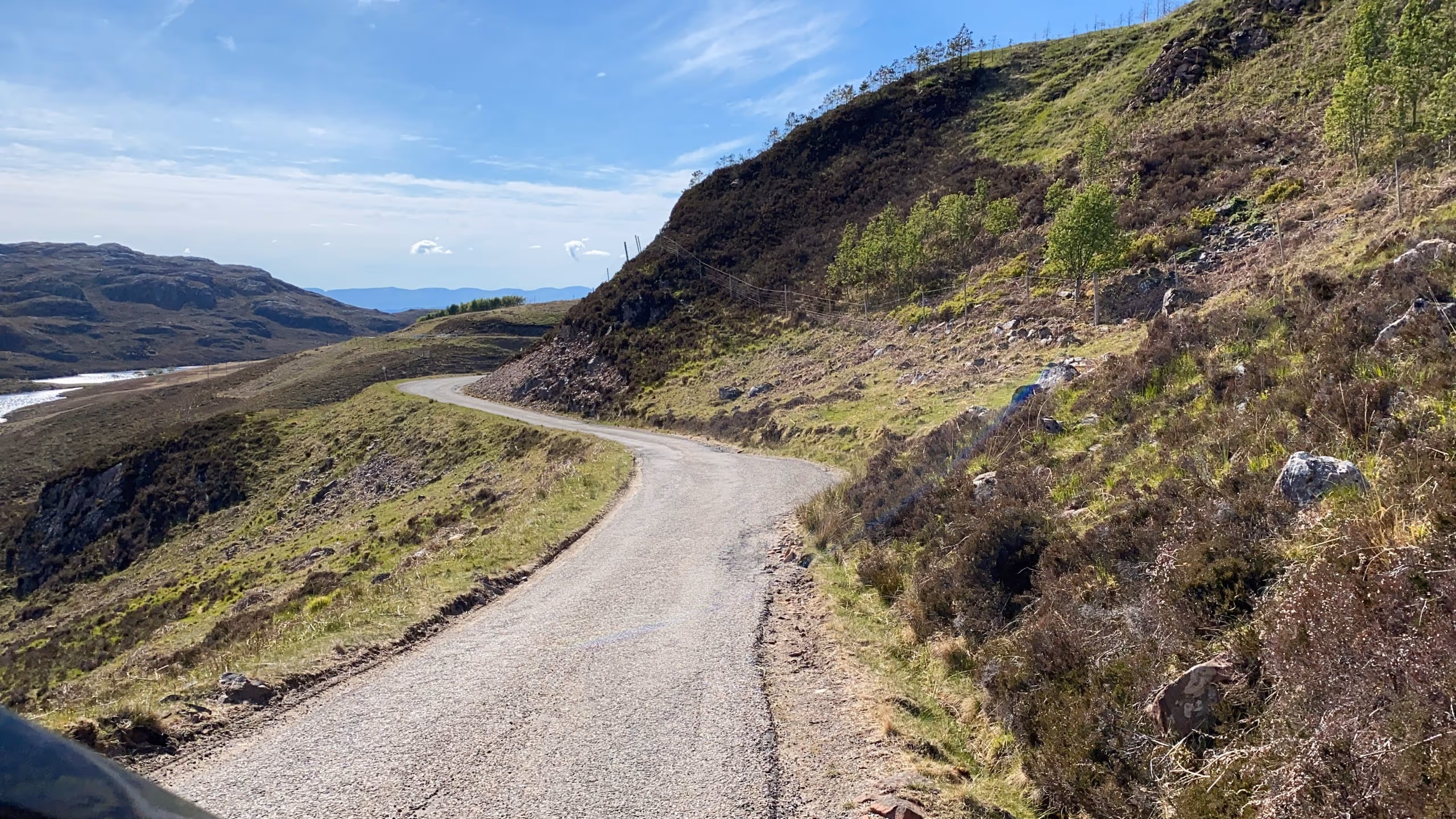 The single-track coast road on the Applecross peninsula curving round a green hillside high above the sea