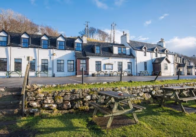 The Applecross Inn, a low white building on the shore with picnic tables out on the grass in front of it