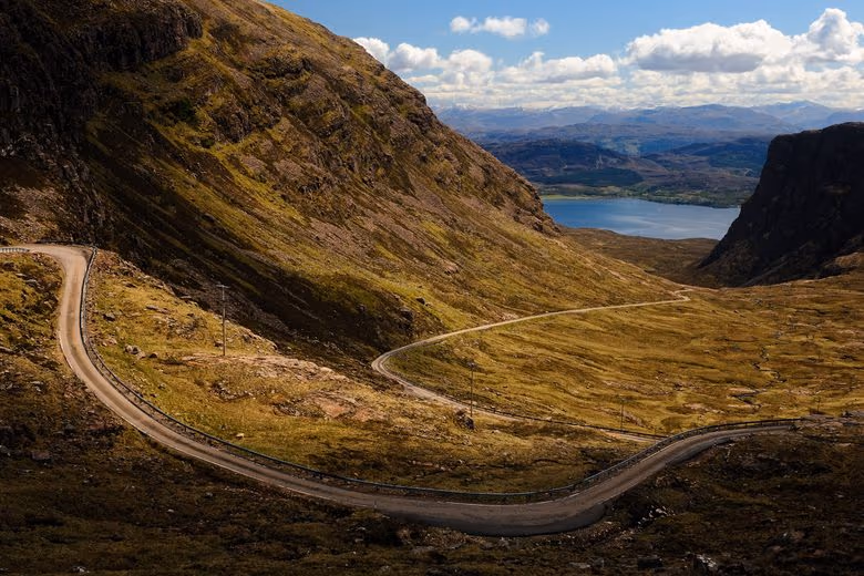 The Bealach na Bà climbing across the hillside in single track, the loch below it and the hills of Torridon beyond
