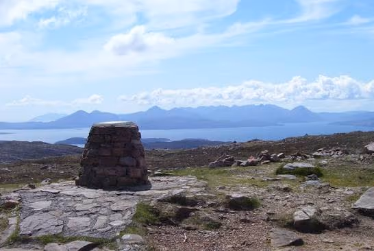 The cairn at the summit of the Bealach na Bà, Raasay and the hills of Skye laid out across the Inner Sound behind it