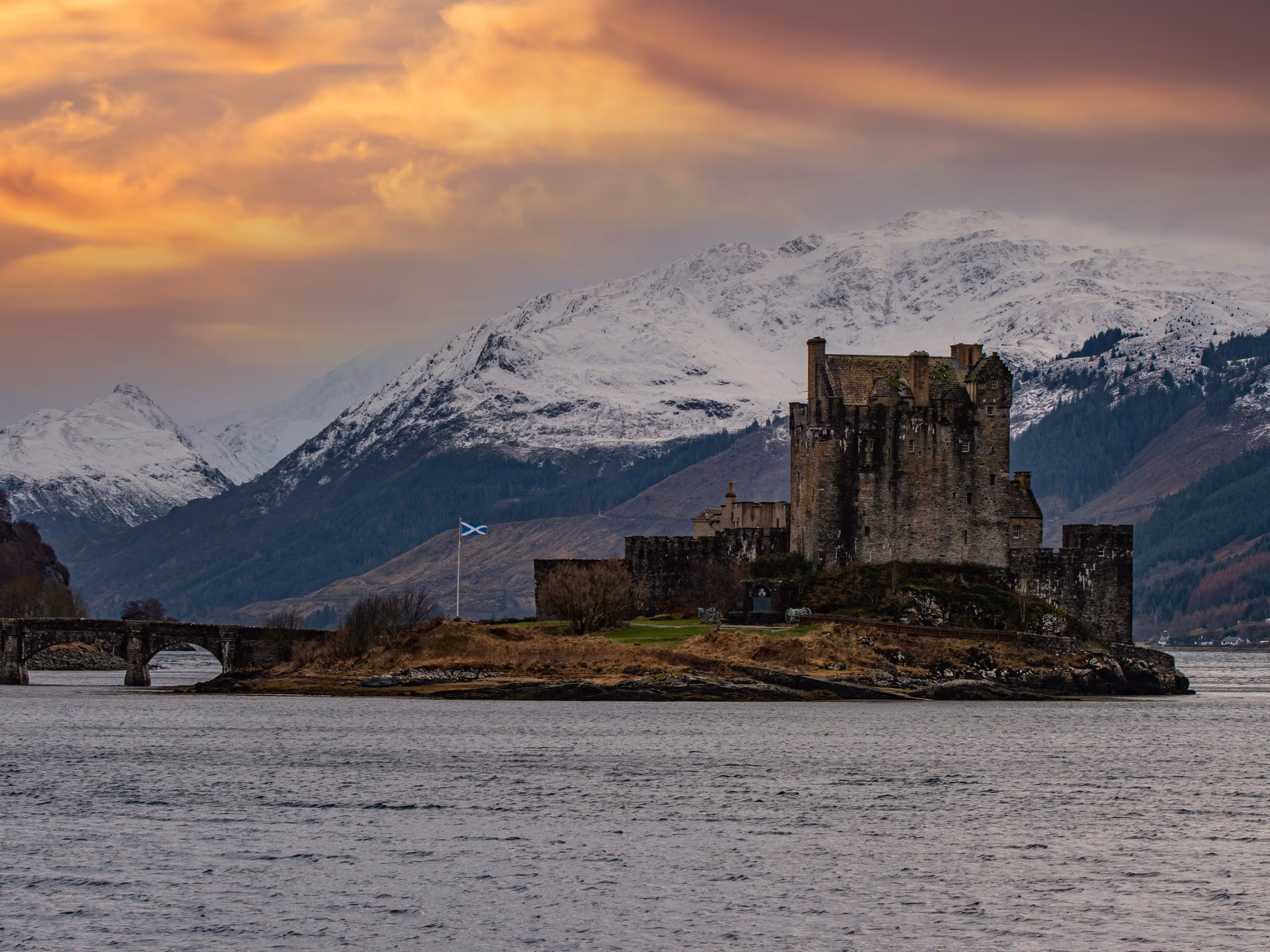 Eilean Donan castle on its island at Dornie, snow across the hills behind it and the sky going gold over the loch