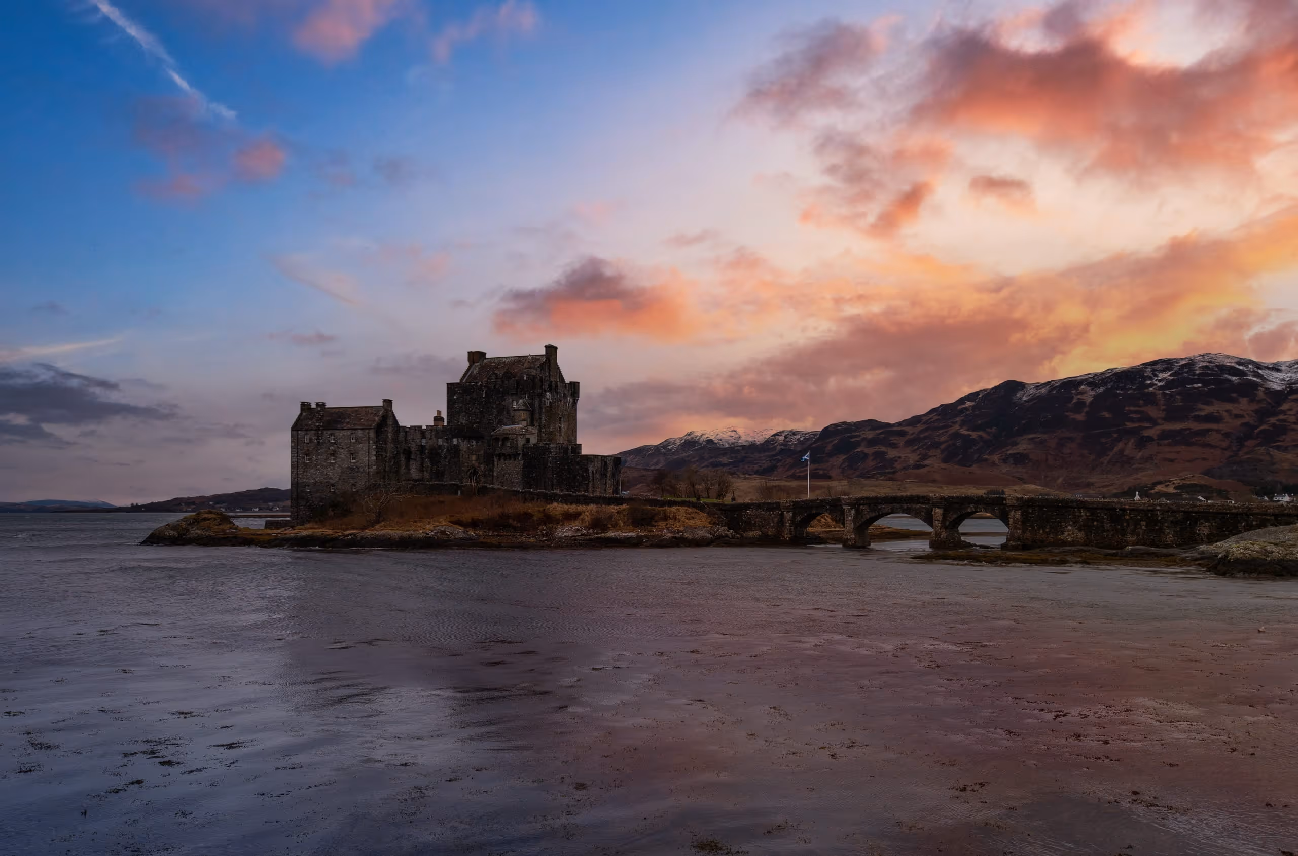 Eilean Donan and its bridge dark against a pink sunset, the wet sand of the loch holding the colour of the sky