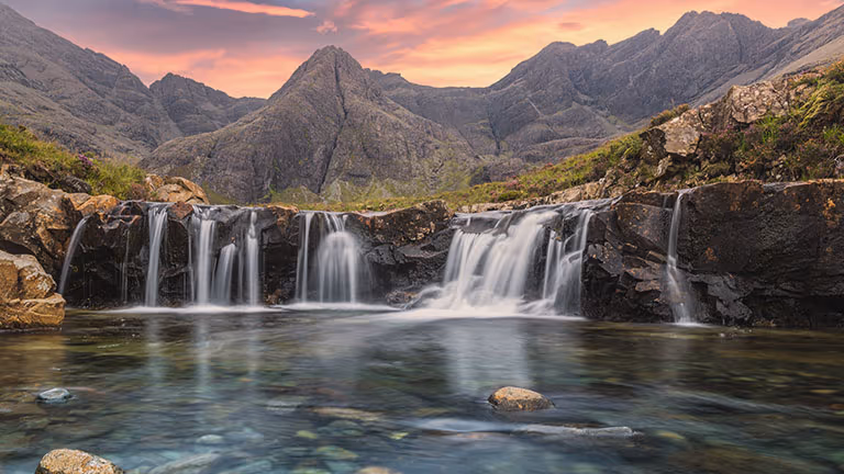 The Fairy Pools falling between rock steps into clear green water, the Black Cuillin ridge dark against the sky behind