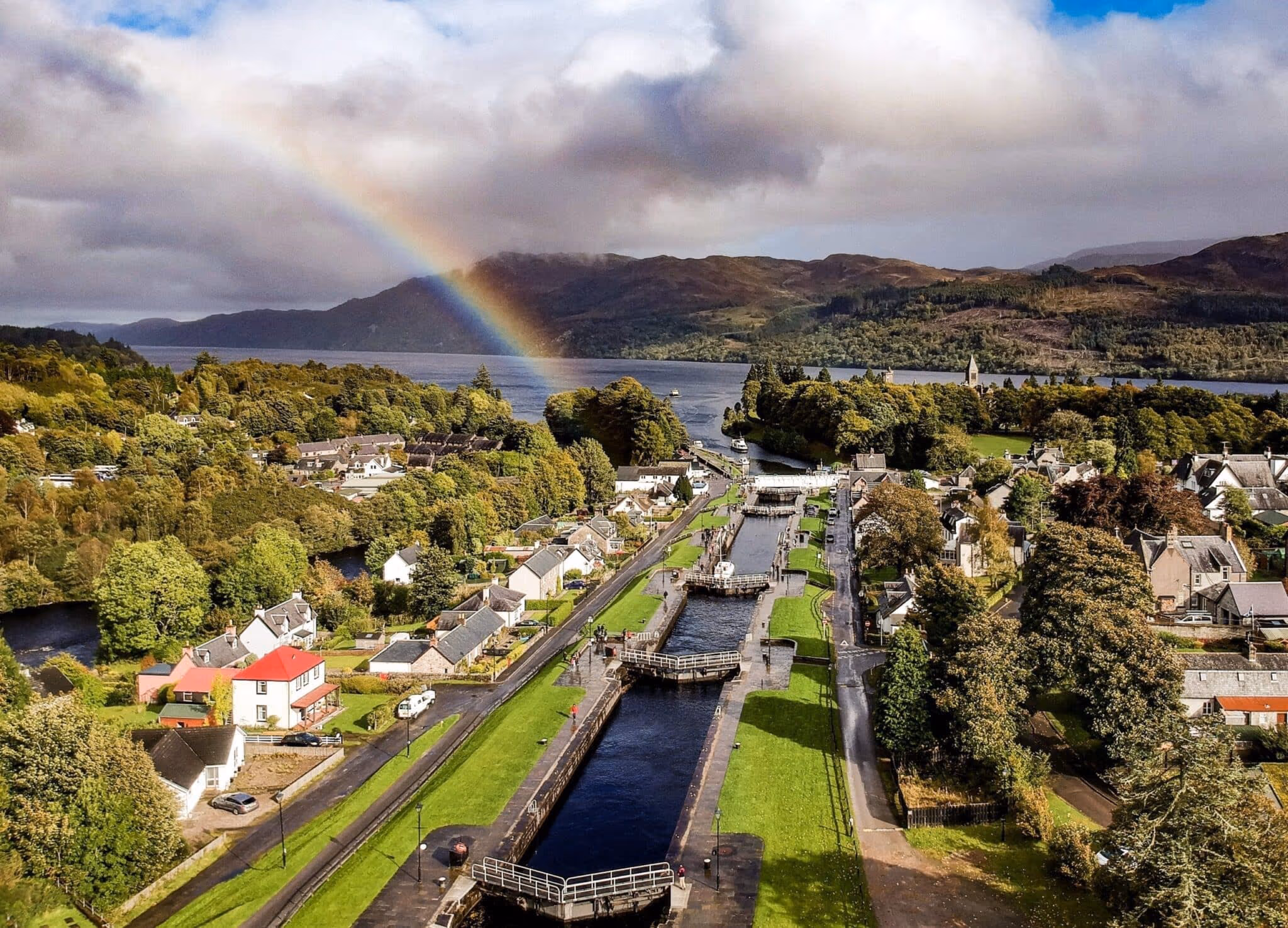 The lock staircase at Fort Augustus climbing away from Loch Ness through the middle of the village, a rainbow over the hills beyond