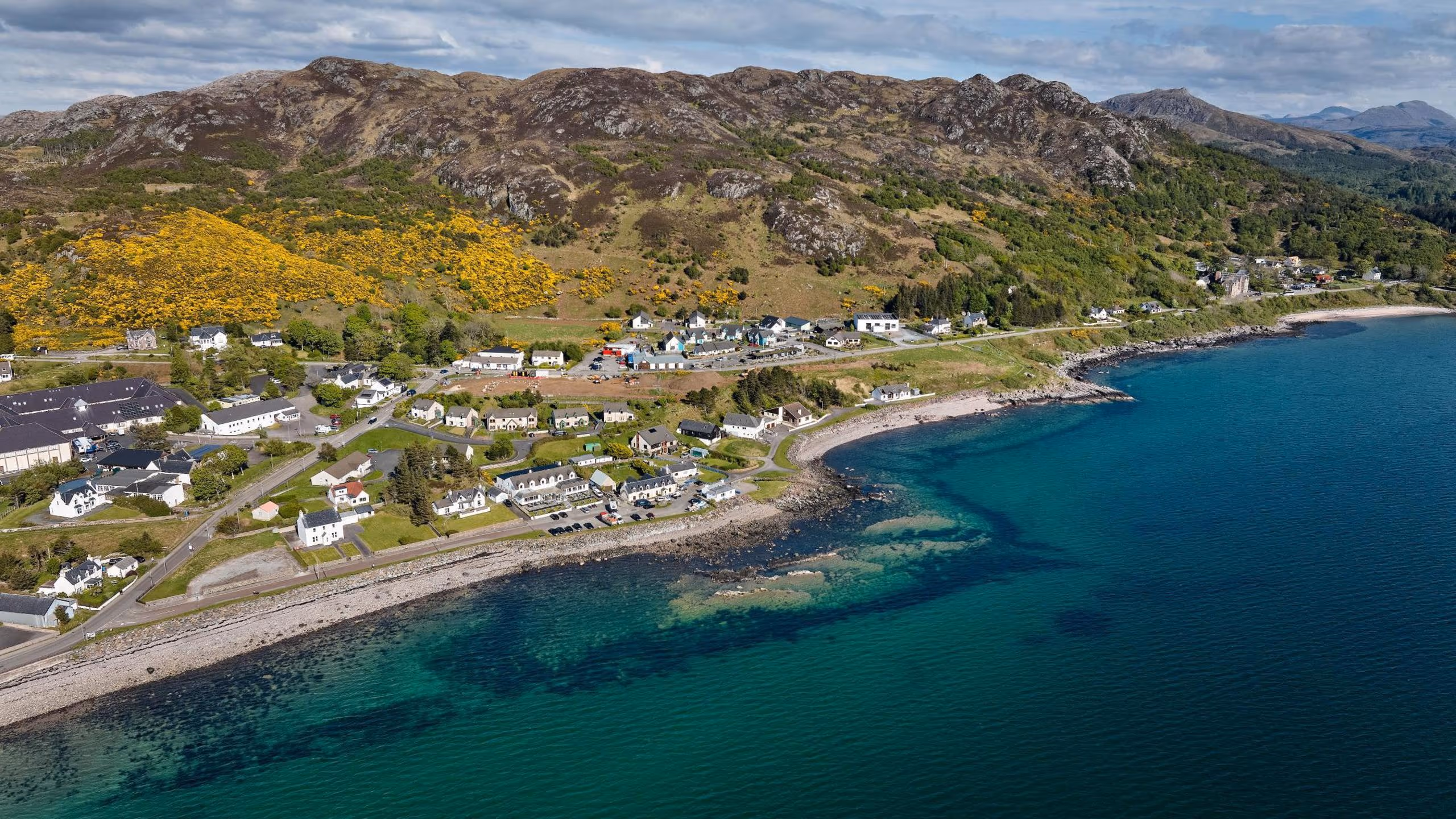 The coast at Gairloch from above, houses along the shore and the water running from turquoise to deep green off the beach