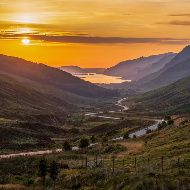 The road dropping down Glen Docherty at sunset with Loch Maree running away between the hills beyond