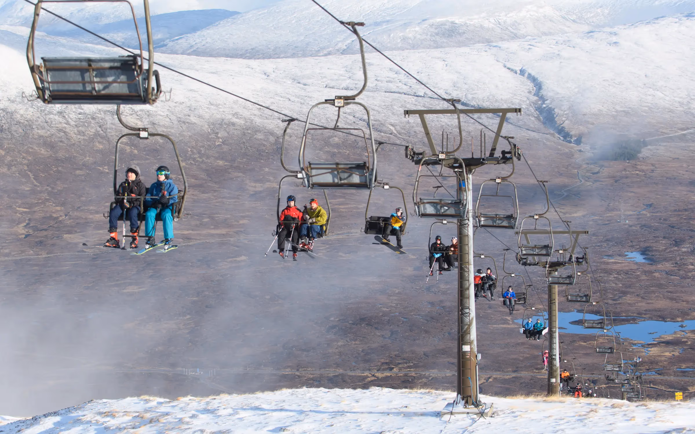 Skiers riding the chairlift at Glencoe Mountain with snow across the tops and Rannoch Moor spread out below