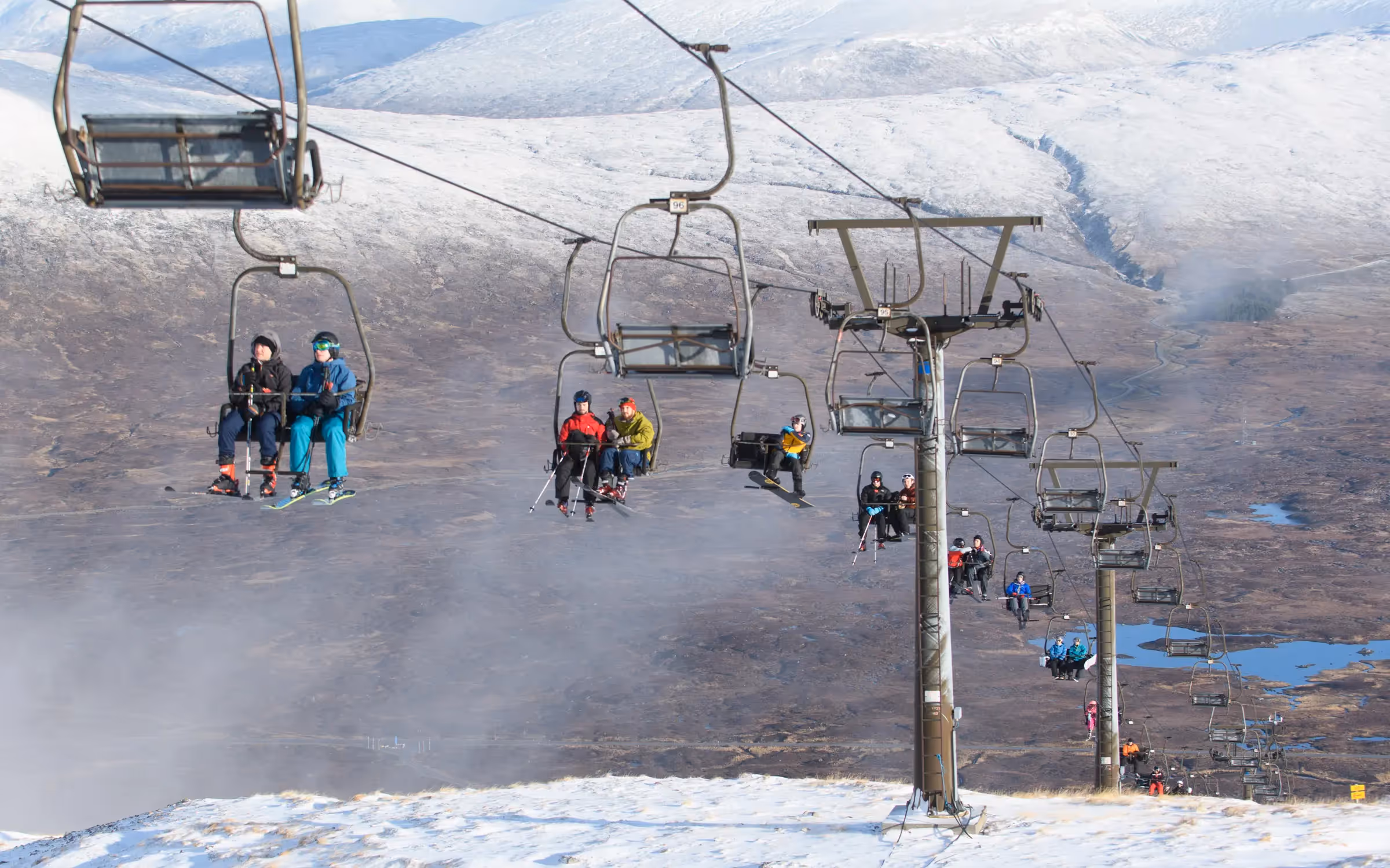 Skiers riding the chairlift at Glencoe Mountain with snow across the tops and Rannoch Moor spread out below