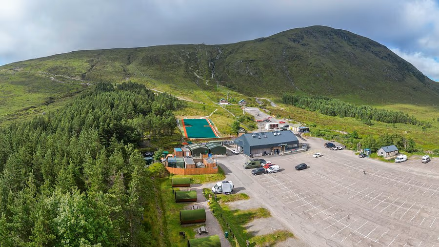 Glencoe Mountain Resort from above in summer, the base buildings and car park with the hill rising green behind