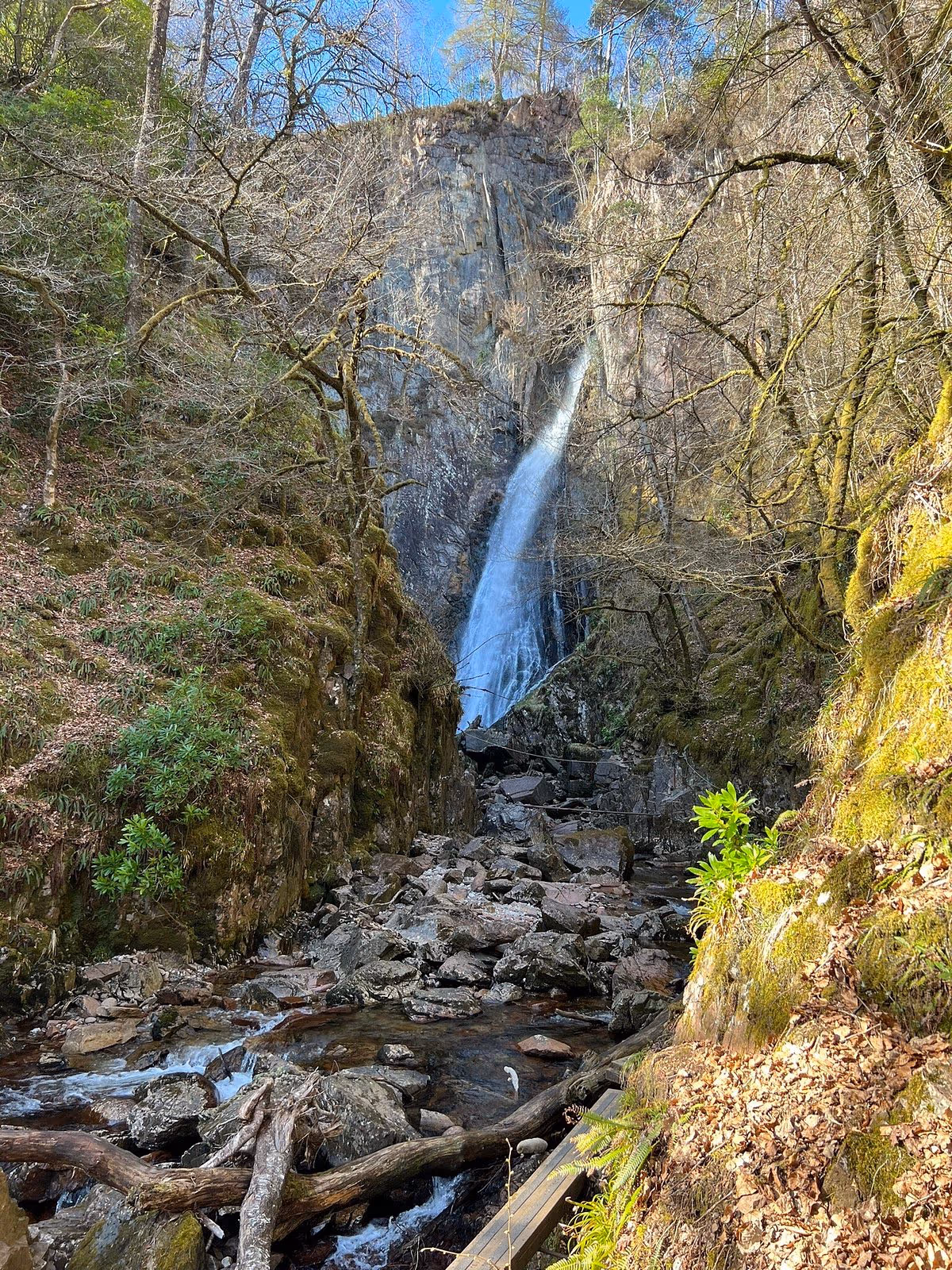 The Grey Mare’s Tail falling down a mossy cleft in the rock above Kinlochleven, bare trees and boulders at the foot of it