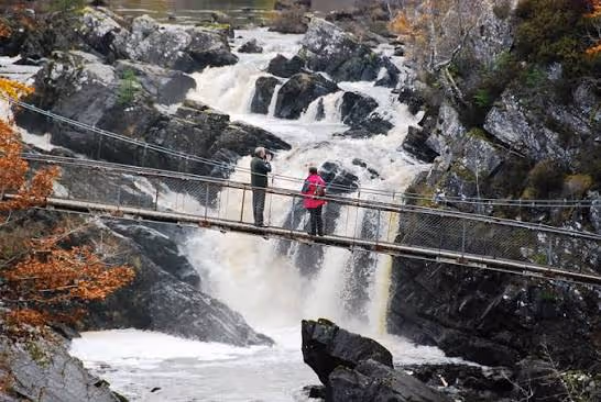 Two people on the suspension bridge over Rogie Falls, the river coming down white through the rocks under them