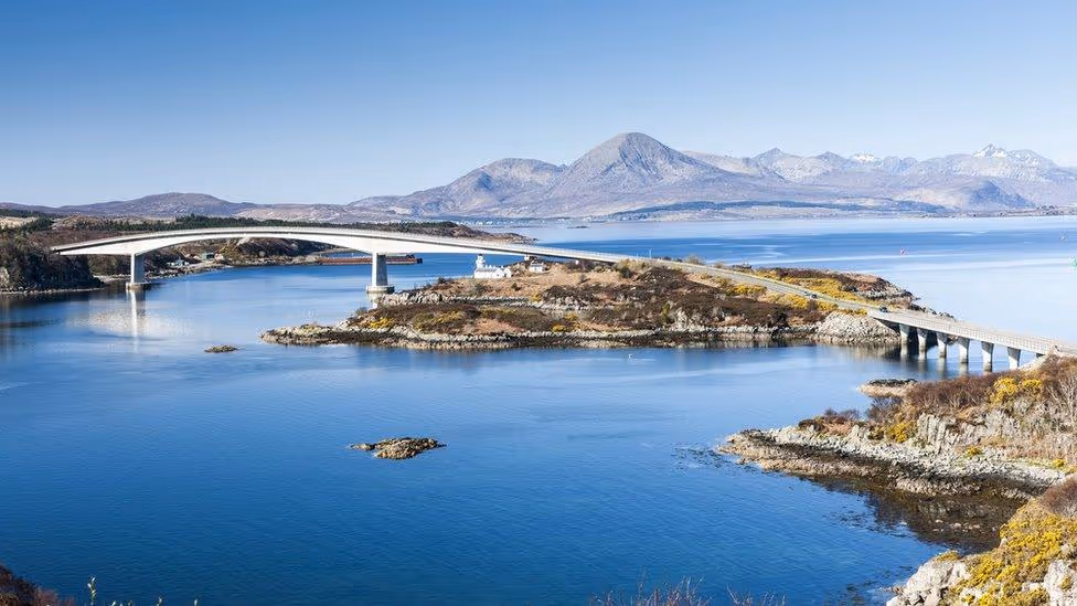 The Skye Bridge curving across from Kyle of Lochalsh, the lighthouse on the island beneath it and the Cuillin beyond
