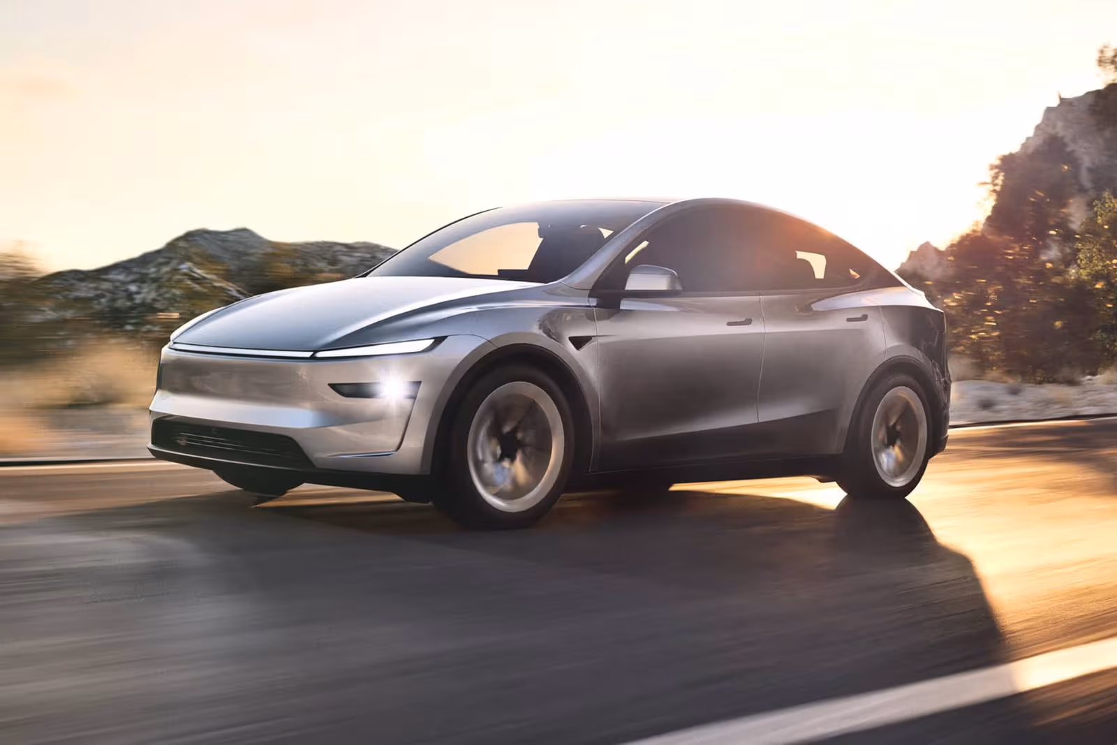 A grey Tesla Model Y on an open road, low sun behind it