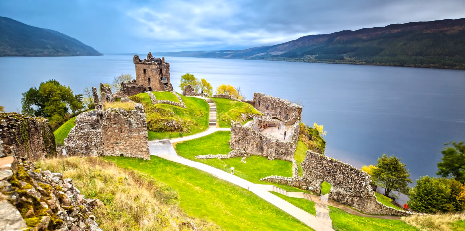 Urquhart Castle on its spur above Loch Ness, the ruins and the green below them almost empty of people, the loch running away north-east