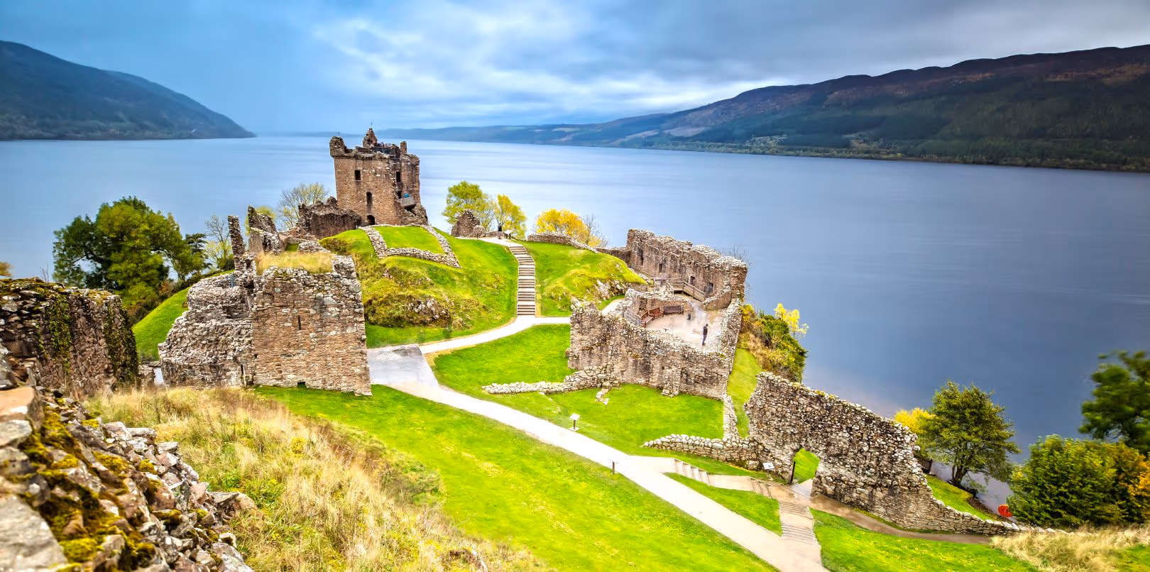 Urquhart Castle on its spur above Loch Ness, the ruins and the green below them almost empty of people, the loch running away north-east