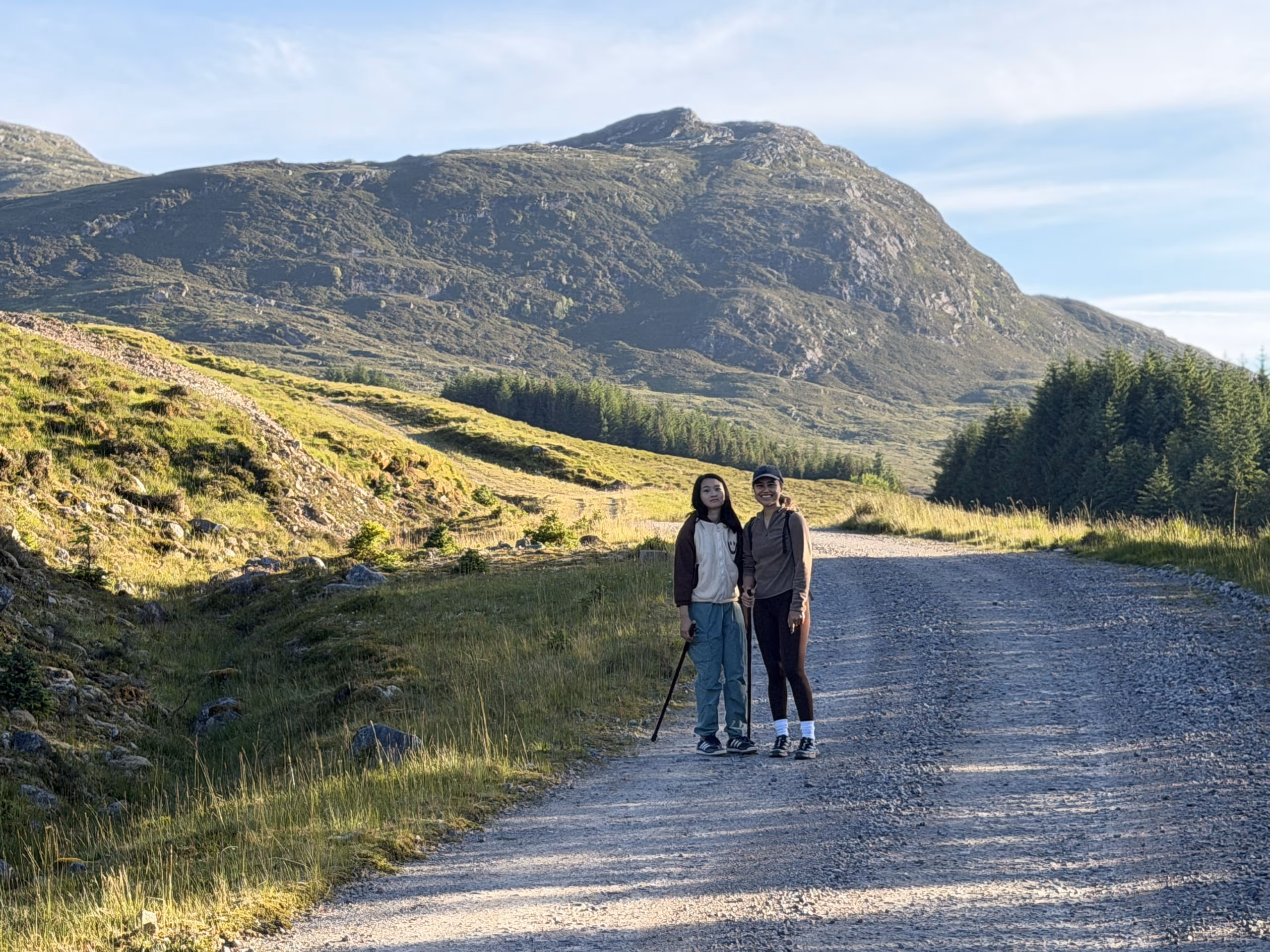 Two walkers on a track above the road west to Skye, green hills and a long ridge rising behind them