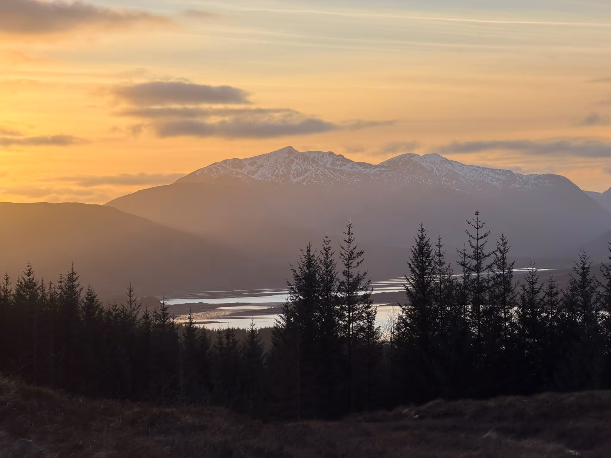 Sunset from the Loch Loyne viewpoint, the loch low and silver between the pines with snow along the ridge beyond